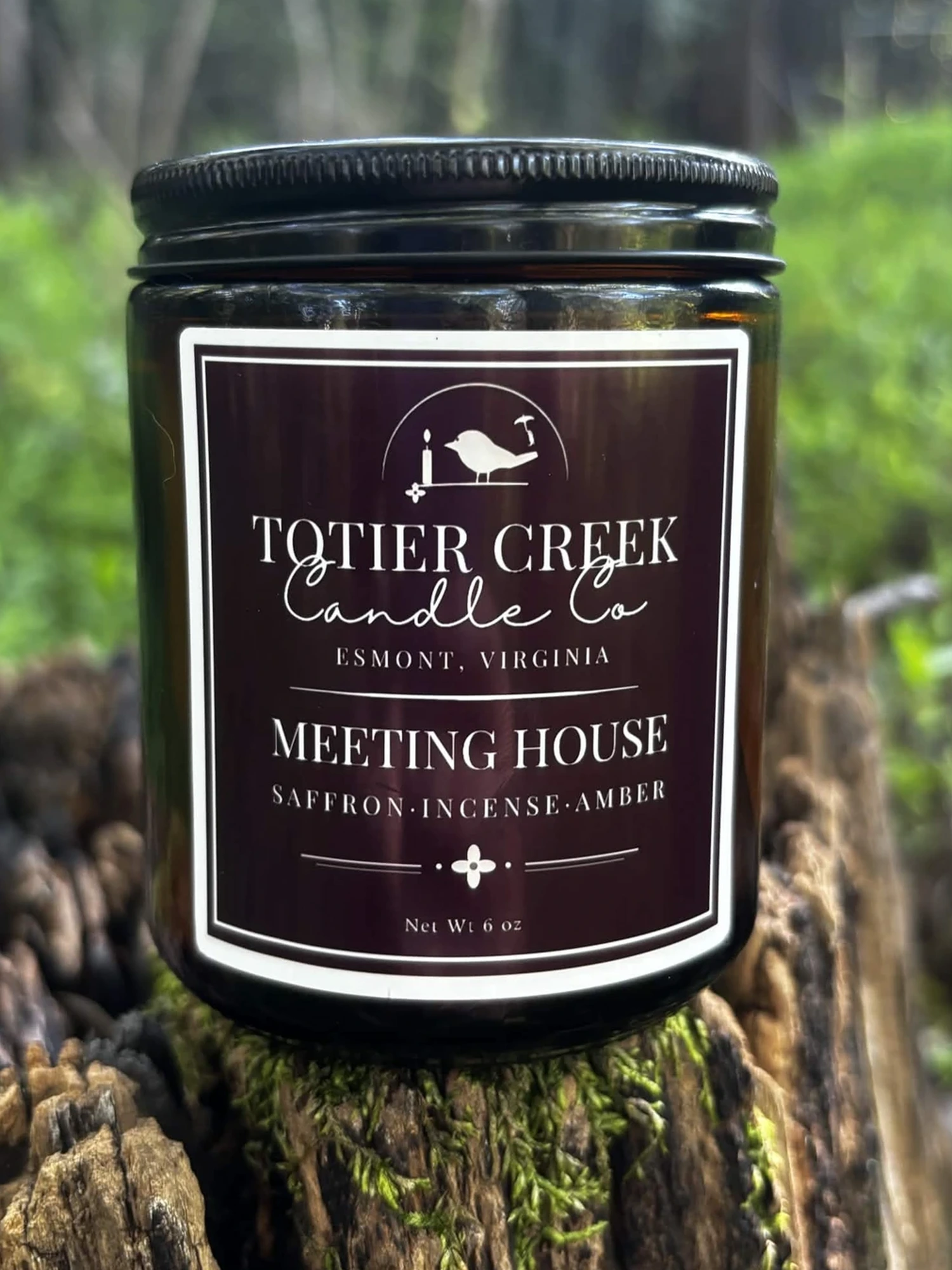 Meeting House candle in an amber jar on a mossy stump in the woods