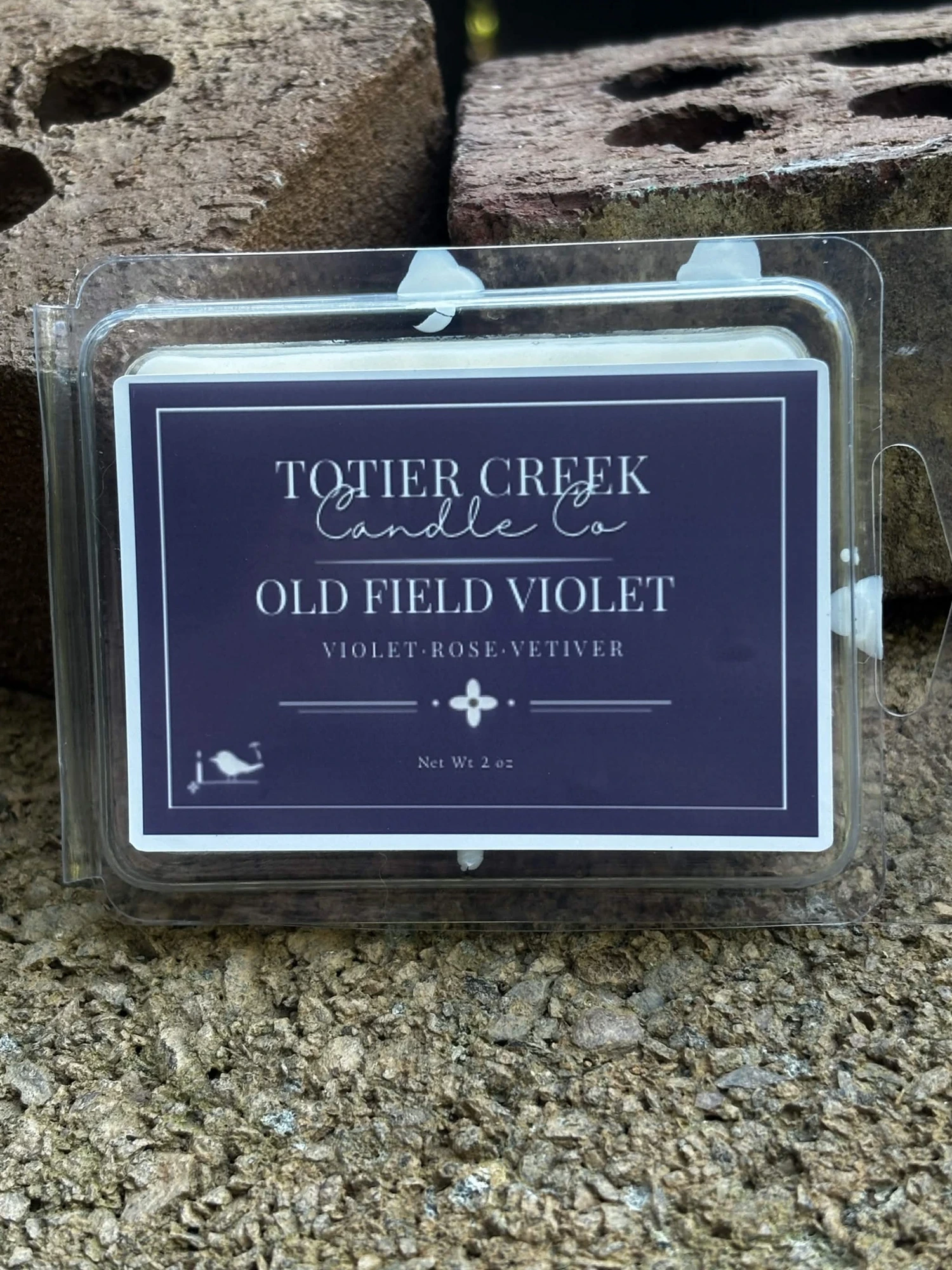 Old Field Violet wax melt in a clear clamshell on creek stone